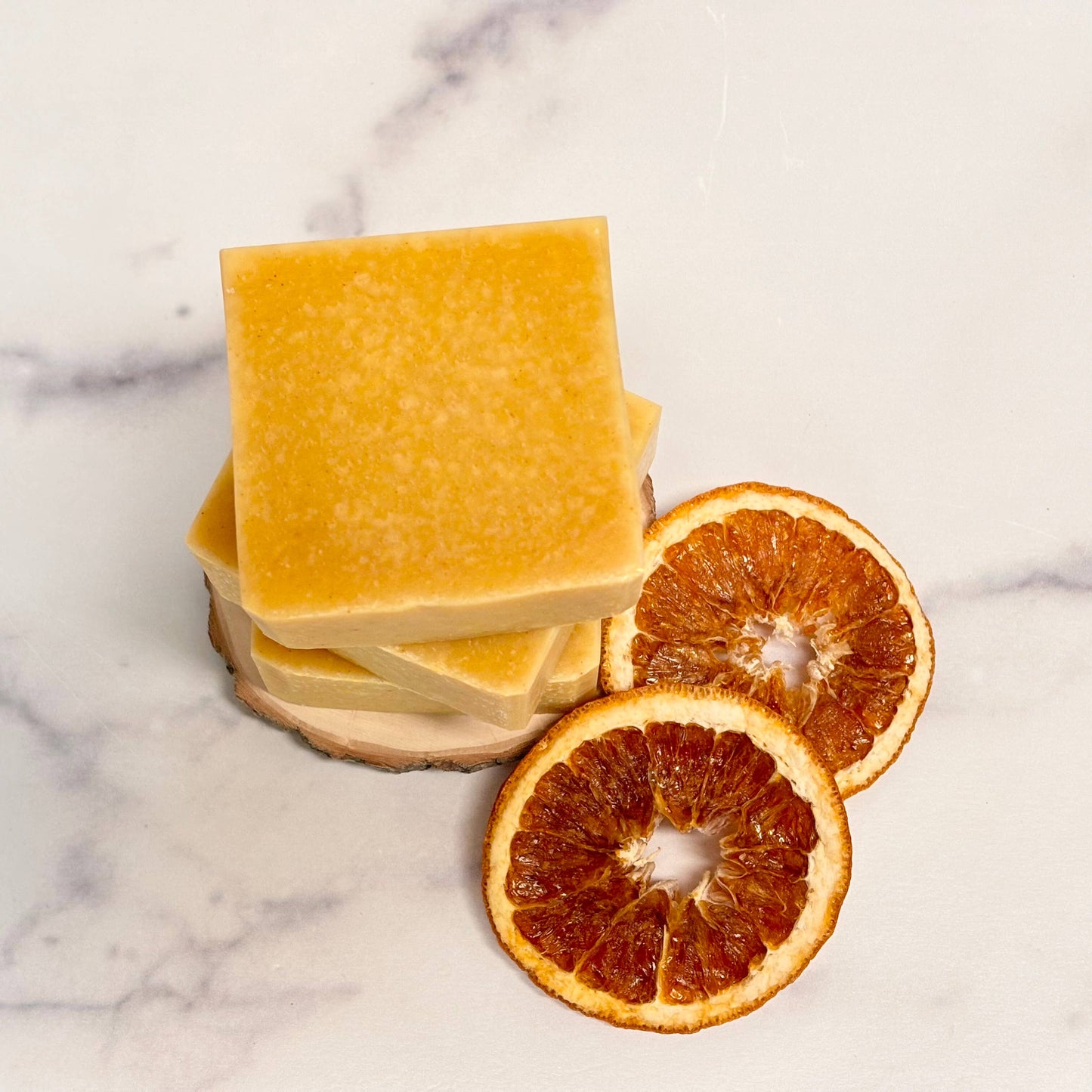 Orange-colored soap bars with orange slices on a marble surface