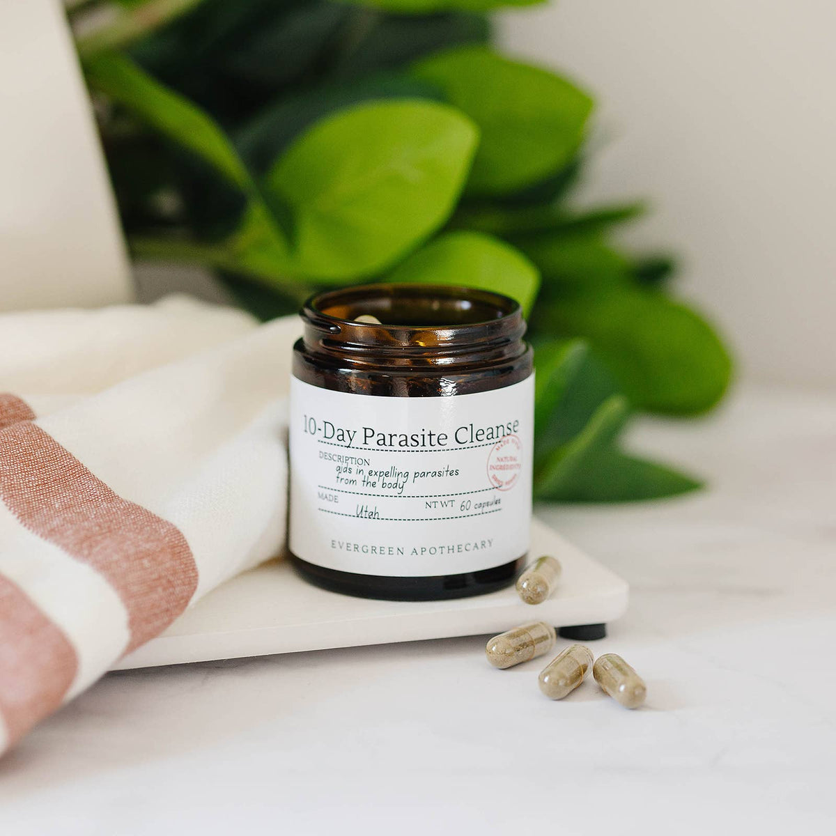 10-Day Parasite Cleanse supplement bottle with capsules on a marble surface with green leaves in the background
