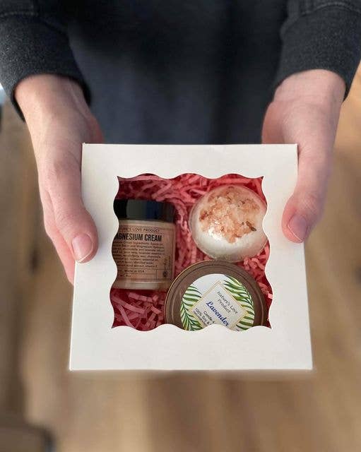 Three small containers of different products in a white box held by hands against a blurred background.