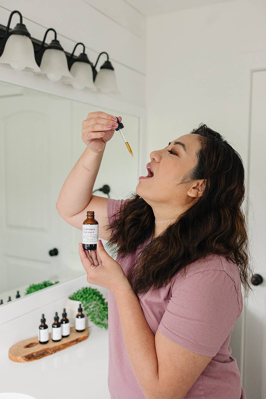 Woman in a bathroom applying a dropper of liquid to her palm.