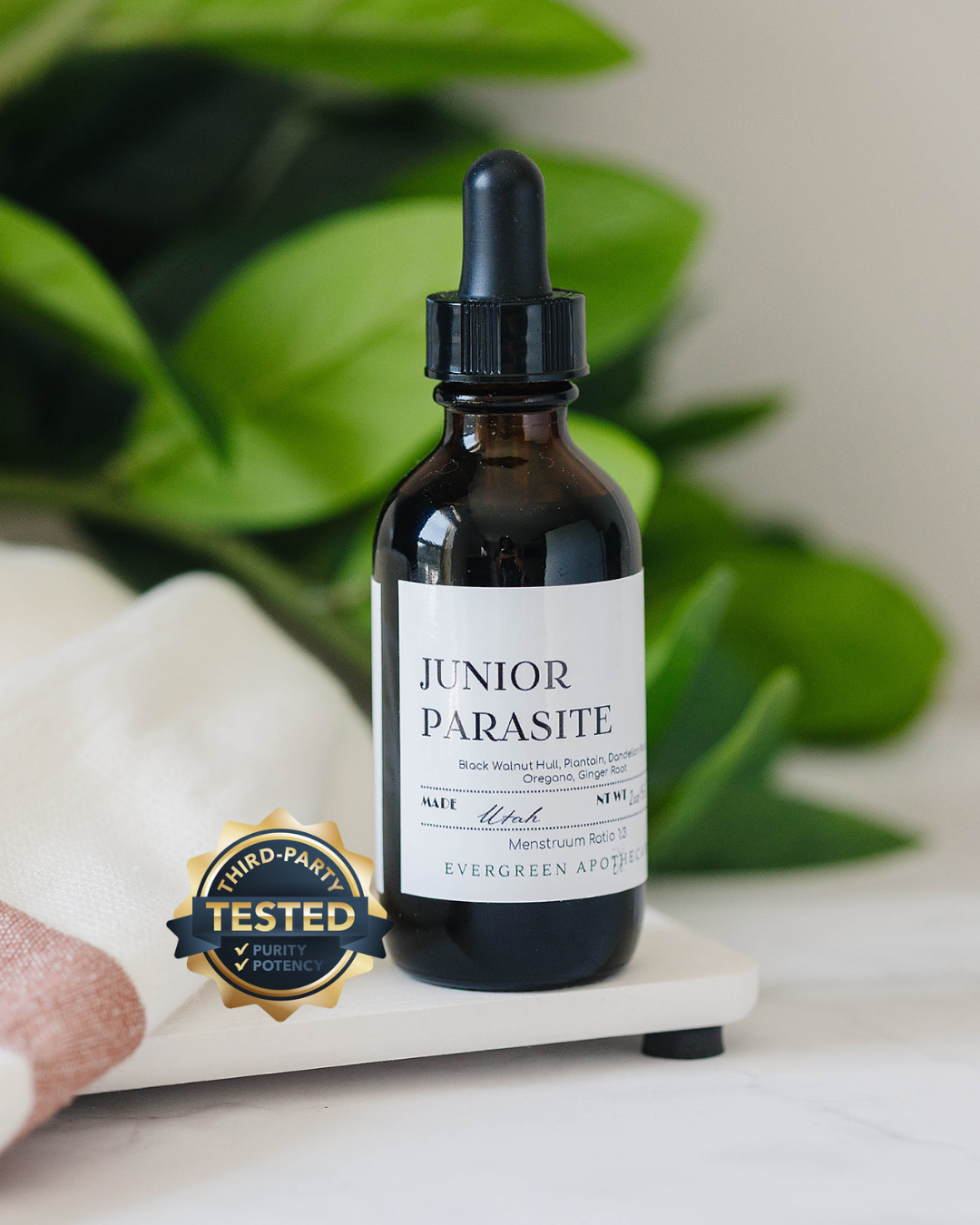 Bottle of Junior Parasite tincture with a dropper on a white surface with green leaves in the background.