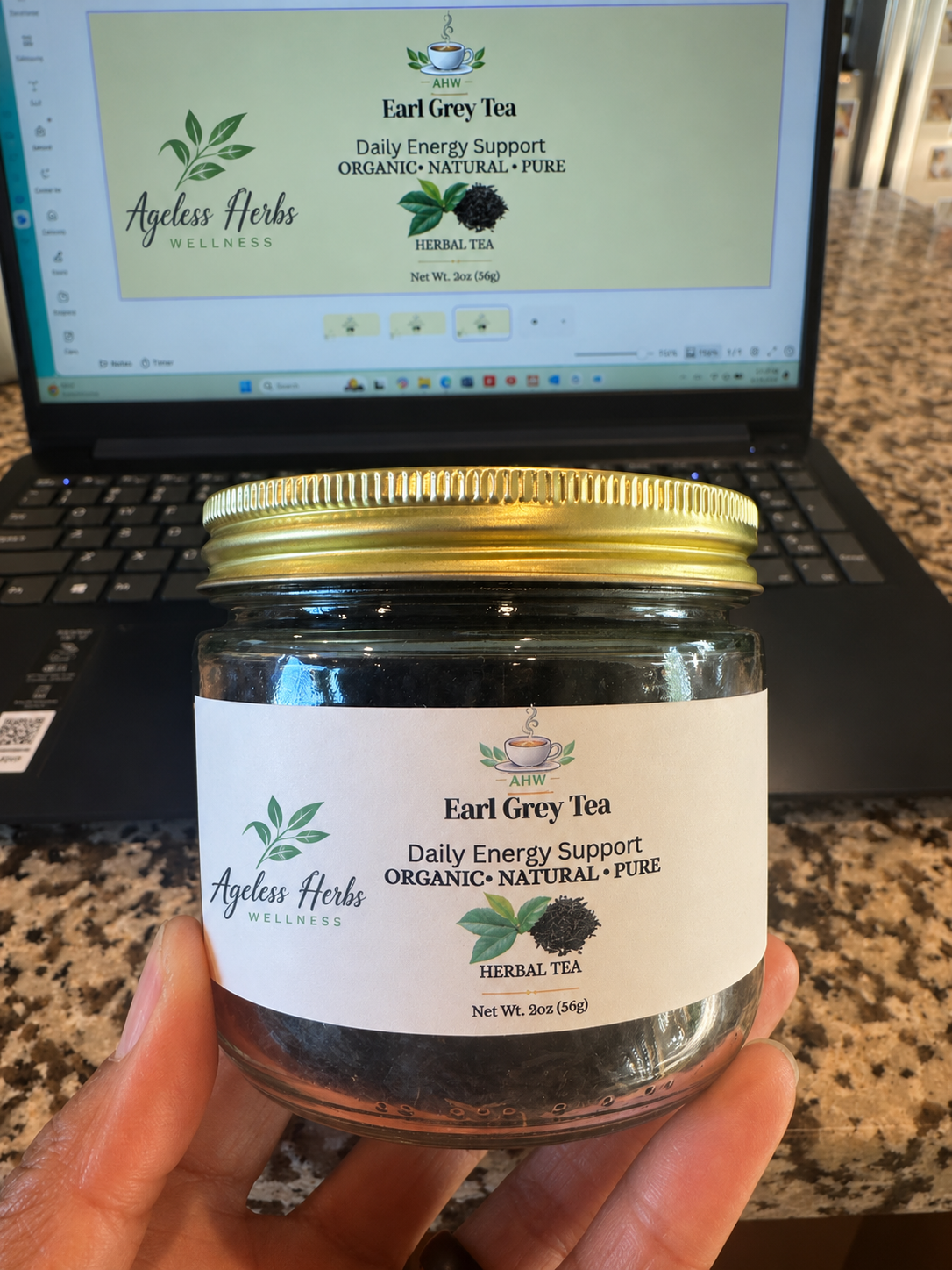 Jar of Earl Grey Tea held in front of a laptop displaying Ageless Herbs website.