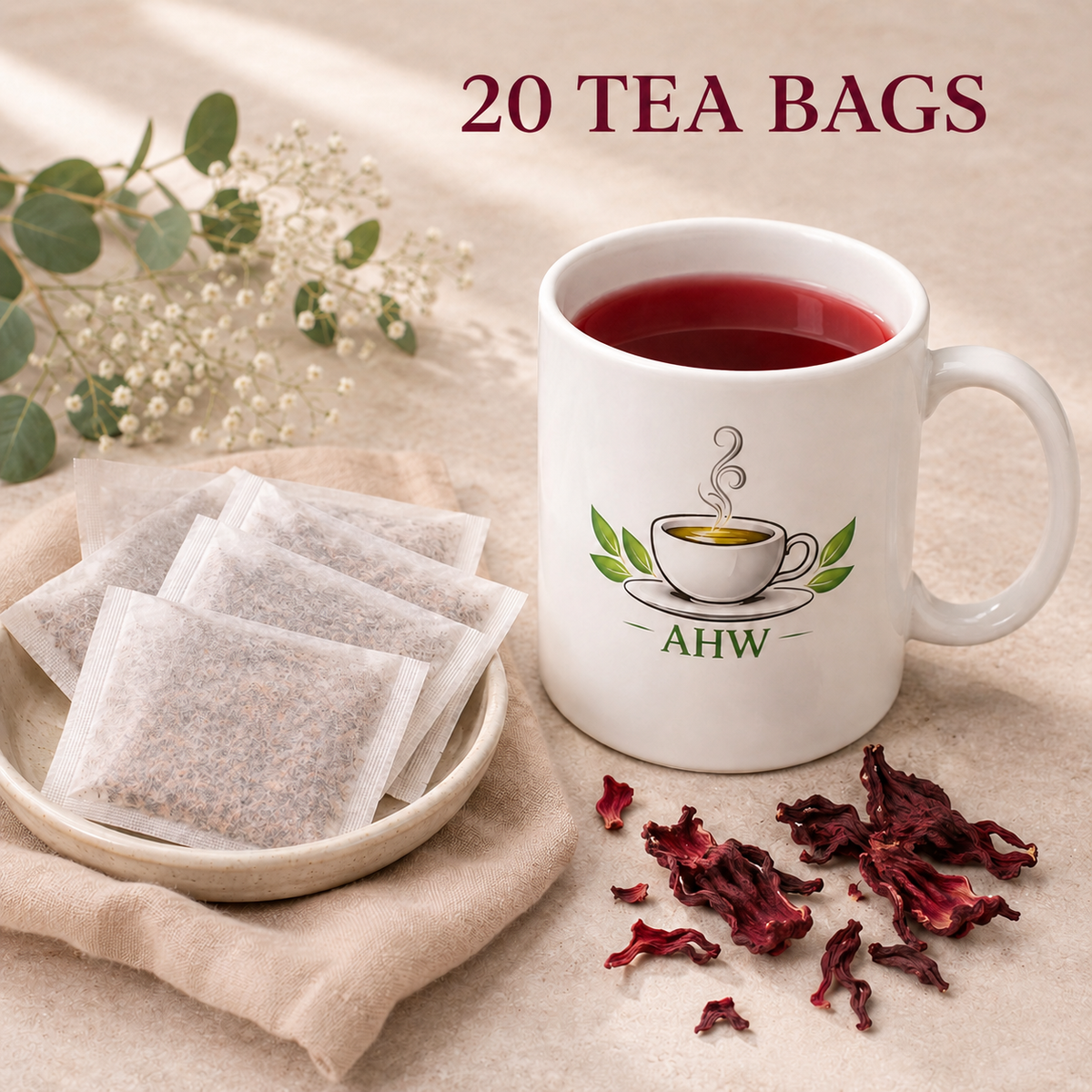 A white ceramic mug filled with dark red tea sits beside a small dish of tea bags and scattered dried red tea leaves on a beige fabric surface. The mug has a green teacup and leaf graphic with the letters AHW.