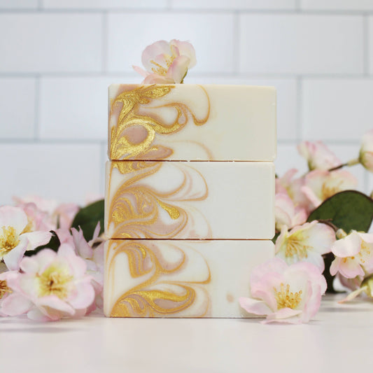 Marble-patterned soap bars with gold accents on a white background with flowers.