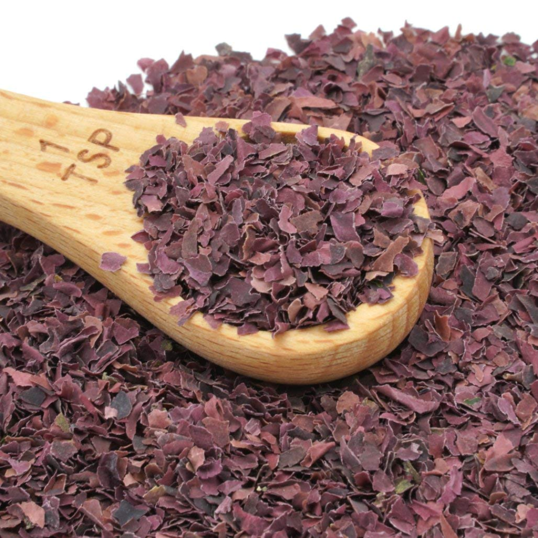Wooden spoon filled with dried purple herbs on a white background