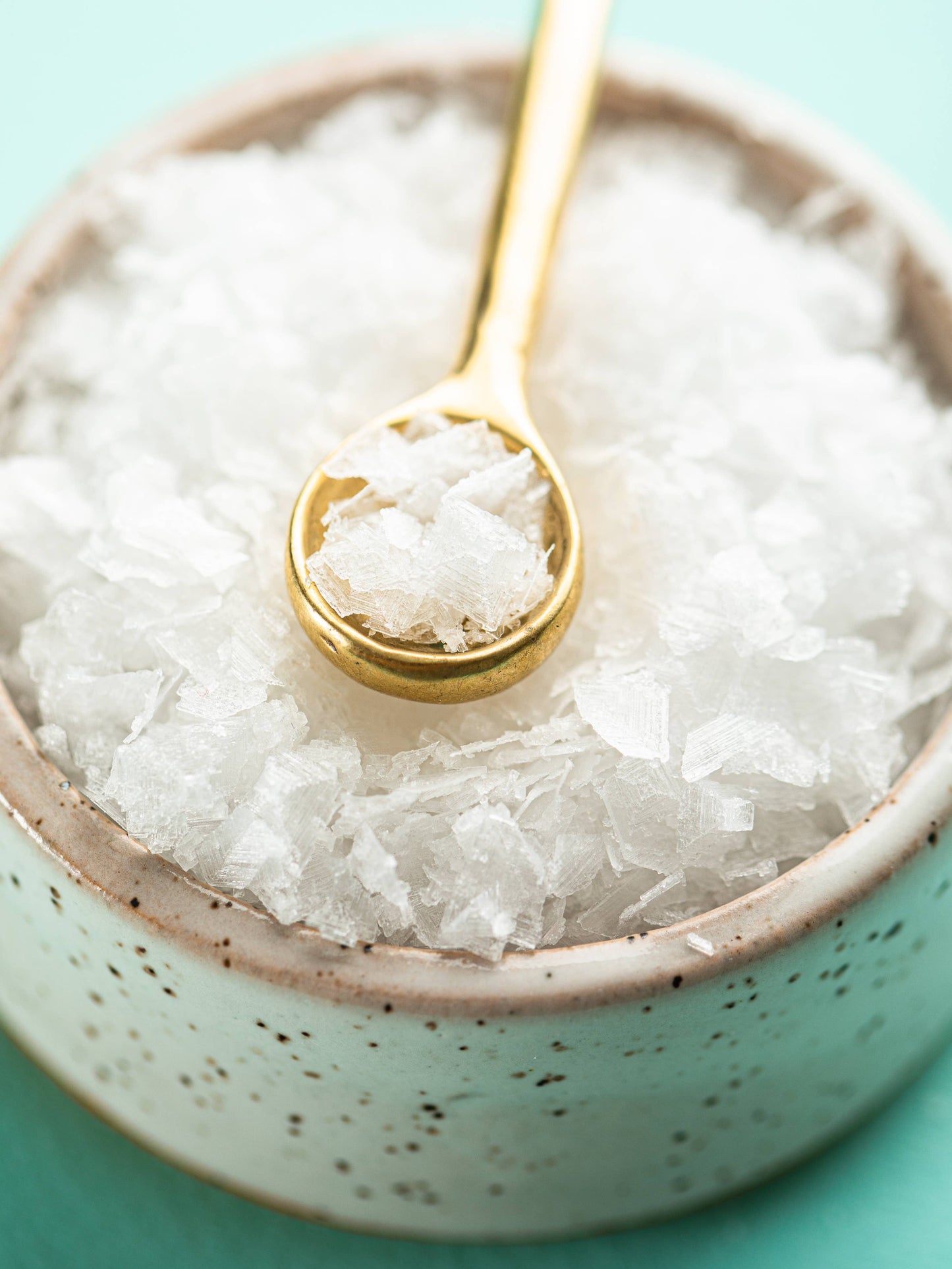Gold spoon in a bowl of white granulated sugar on a teal background